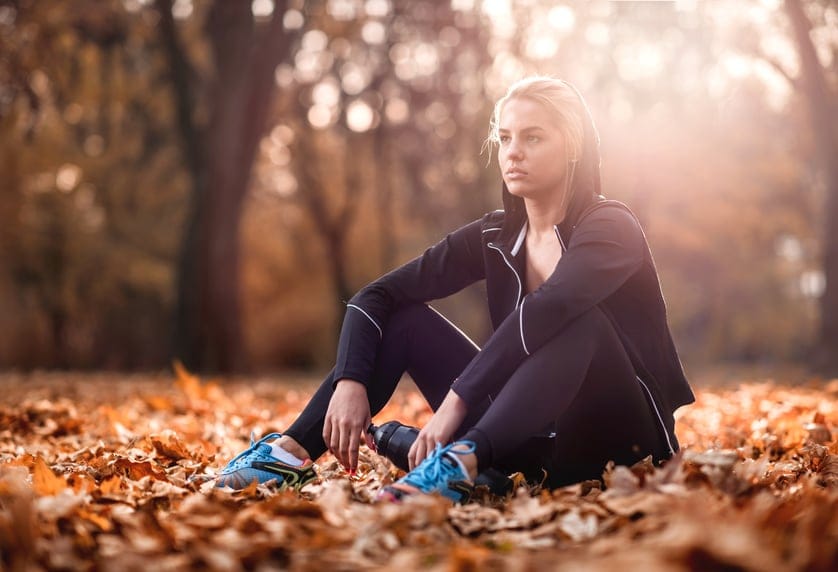 Young pensive woman resting after having a sports training during autumn day in the park.