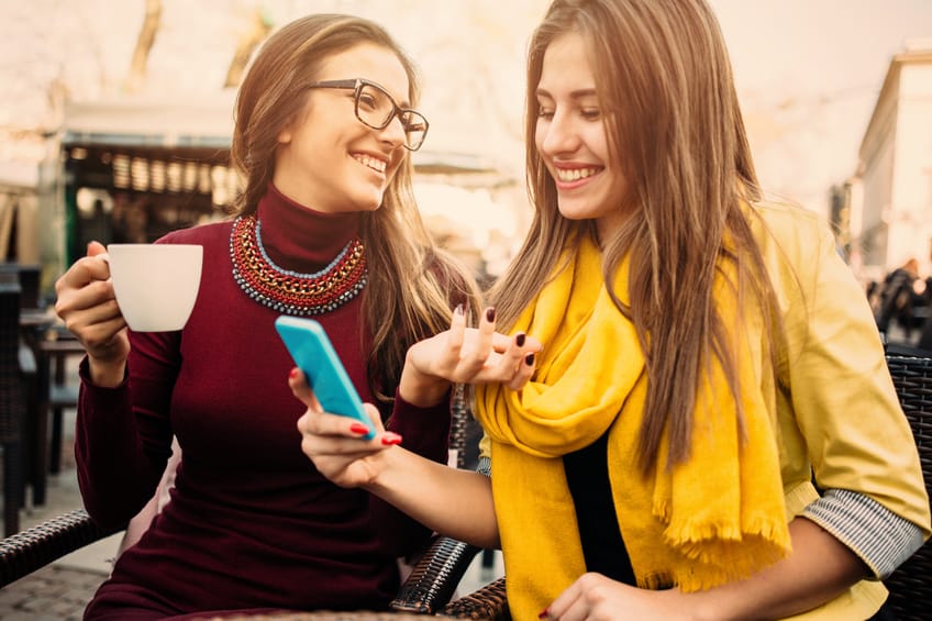 Two beautiful girls sitting at a city cafe and using a smart phone.