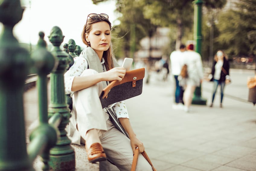 Smiling businesswoman is using her smart phone in the city.