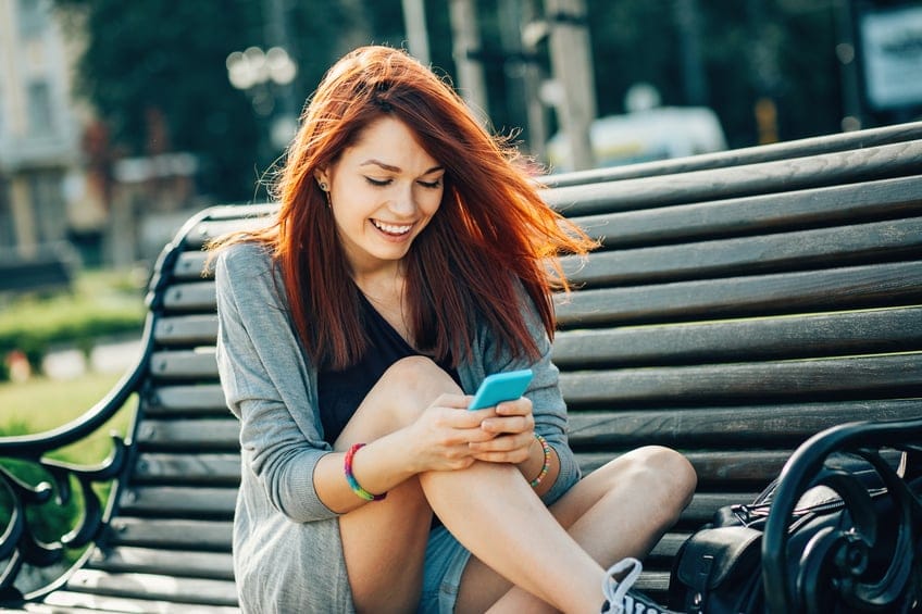 woman texting phone park bench