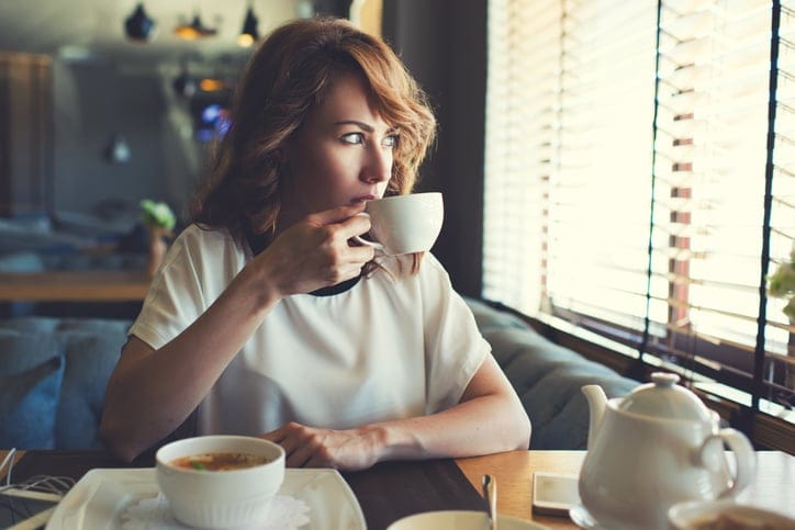 Portrait of young gorgeous female drinking tea and thoughtfully looking out of the coffee shop window while enjoying her leisure time alone,