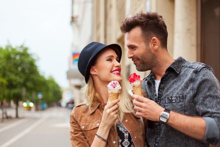 Affectionate couple eating ice cream in the city, looking at each other and smiling. Close up of faces.