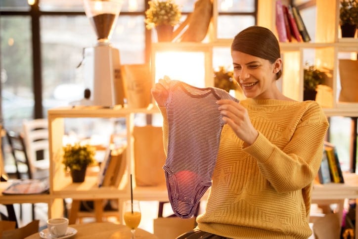 Happy expecting mother in a cafe looking at new baby clothes she has bought.
