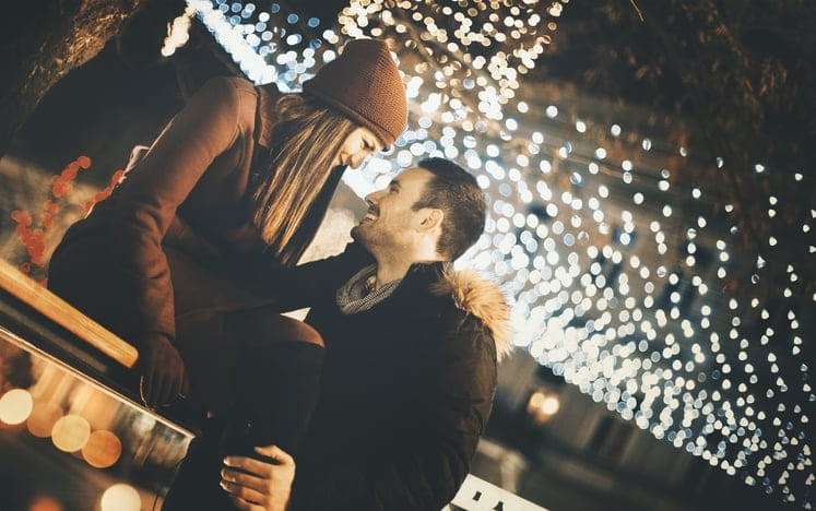 Couple winter night having fun while taking a walk. They are having a sincere laugh with many glittering Christmas lights around them.
