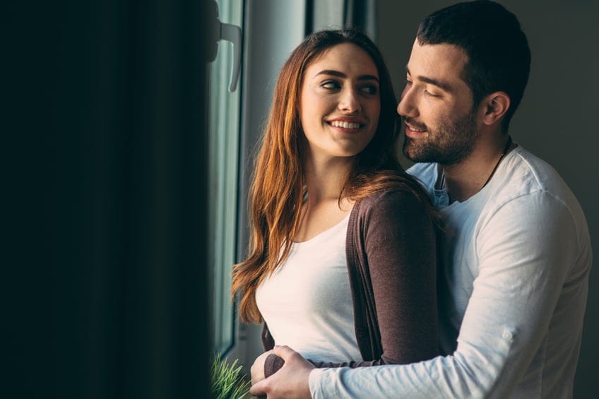 Husband and wife hugging next to the window.