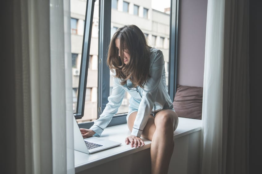 Woman sitting on the windowsill in a hotel room and working on her laptop.