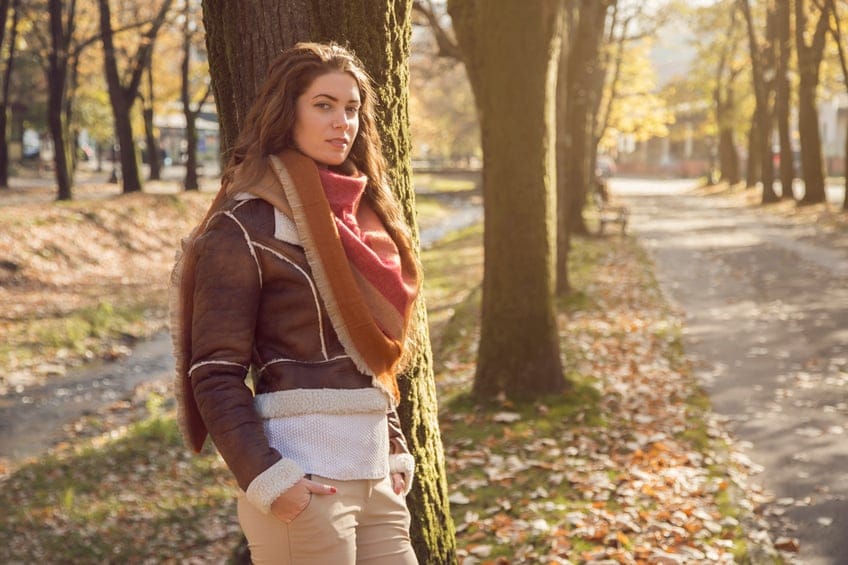Beautiful, young, caucasian woman standing in the park, and leaning on the tree