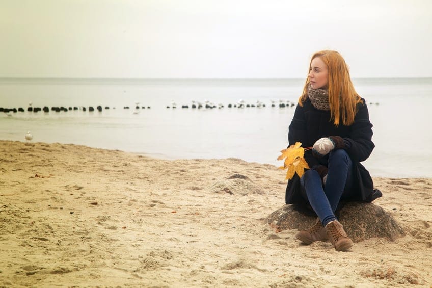 sad pensive woman on autumn sea beach sitting, toned image