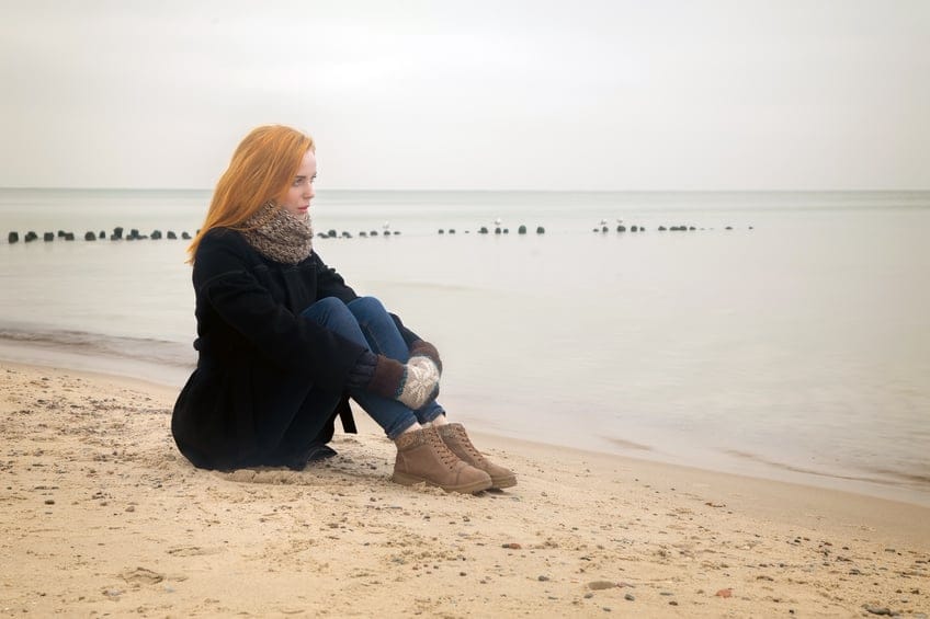 sad pensive woman on autumn sea beach sitting, toned image