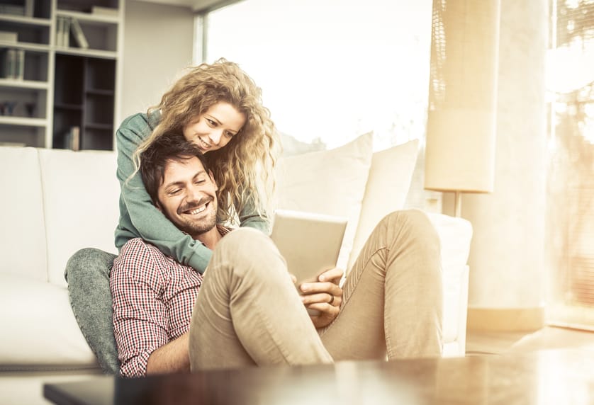 Couple of lovers at home watching the smartphone on the couch - Man and woman relaxing of the sofa, woman leaning head on her boyfriend's shoulder