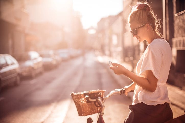 young woman bike phone texting sun summer