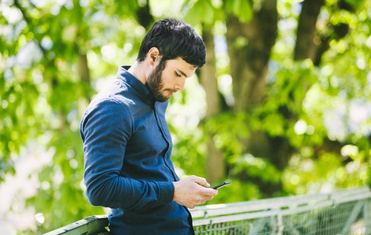 Man reading his phone alone outside.
