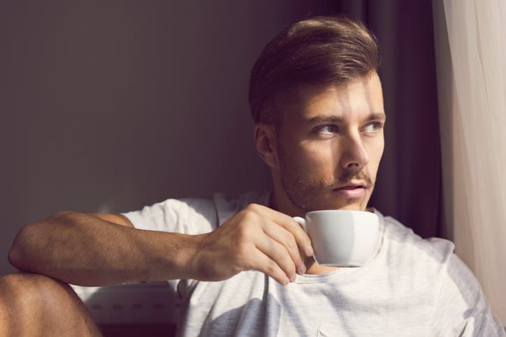 Portrait of a young caucasian man enjoying the first morning coffee and looking at the window.