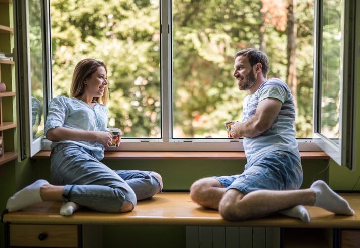 Young happy couple sitting by the window during coffee time and talking to each other.