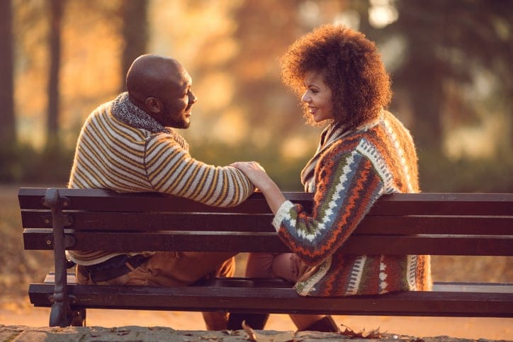 African American couple relaxing on bench and communicating in nature.