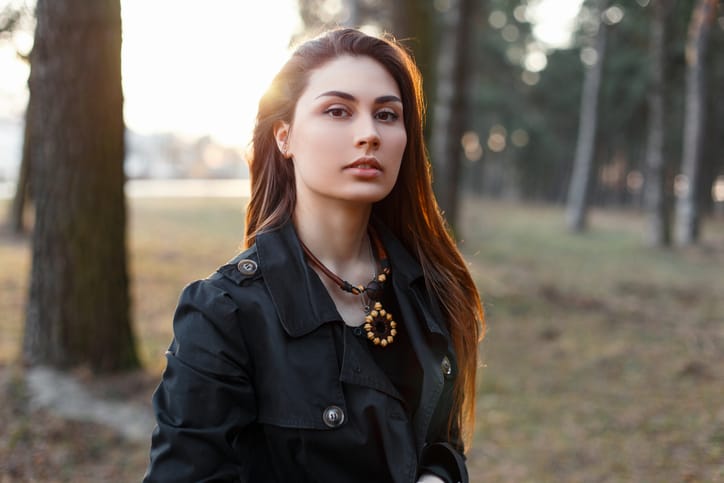 Young stylish girl in a black cloak in the park at sunset.
