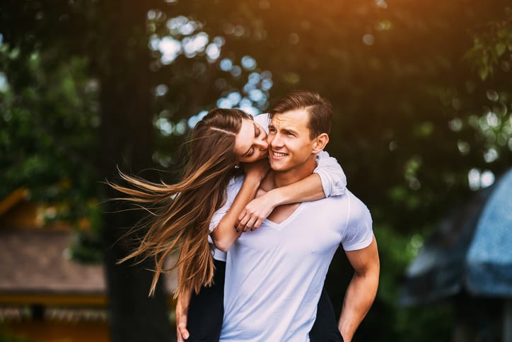 Young man carries his girlfriend on his back in the park