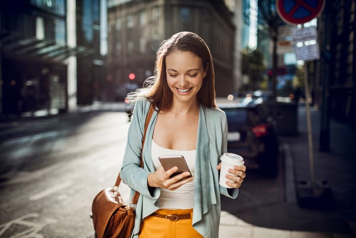 Close up of business woman using a phone while walking and drinking coffee