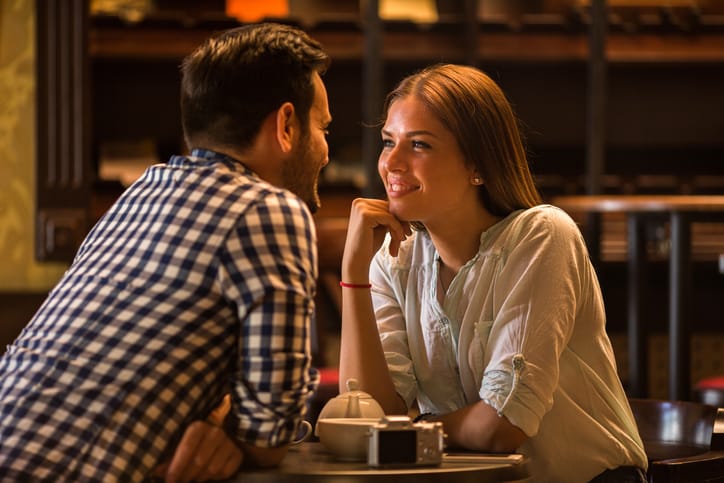 Young smiling woman enjoying in a cafe and talking to her boyfriend.