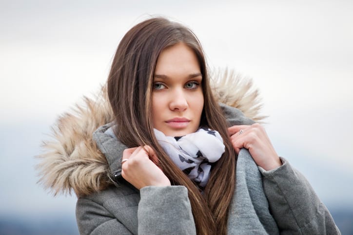 Close-up portrait of attractive young woman in front of blurry background. She is wearing a grey jacket and looking into the camera. Autumn atmosphere, selective focus.