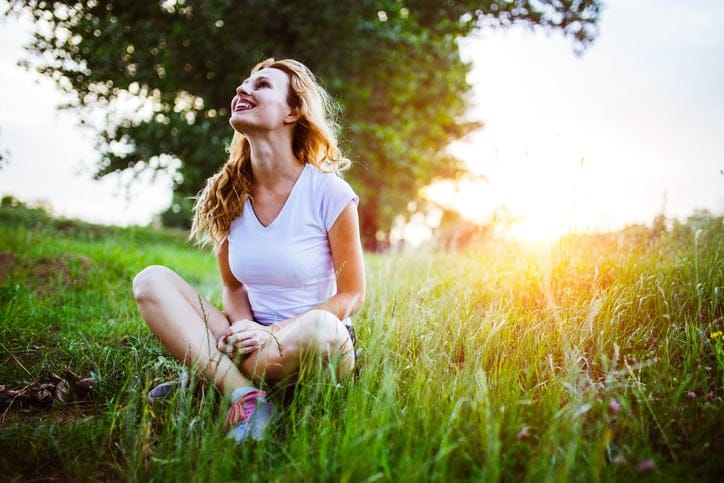 Sensual young woman in the nature, sitting on a green field in sunset.