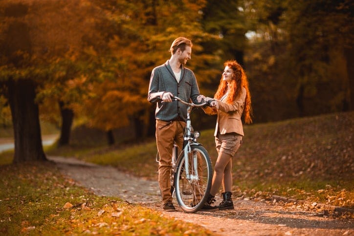 Happy ginger couple talking during autumn day in the park, while man is on bicycle.