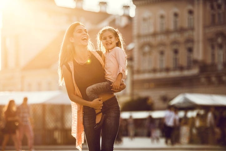 Young happy mother holding her cute little girl and enjoying with her in the city.