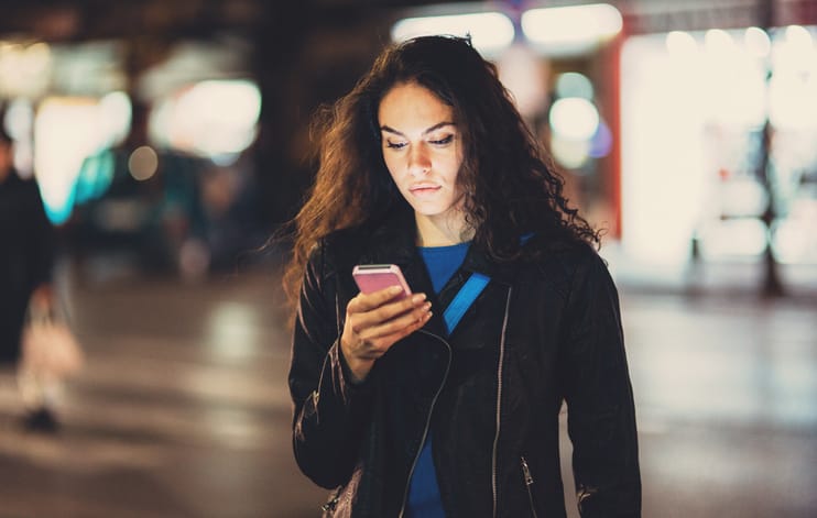 A young woman texting on the phone outdoors at night.