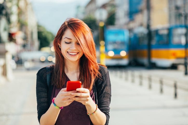 Smiling young woman with smart phone walking outdoors in the city, with copy space