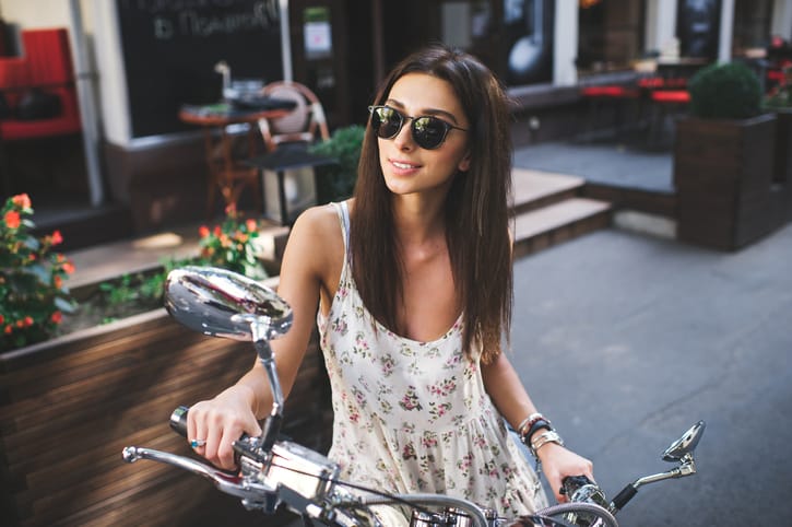 young attractive girl with a beautiful smile wearing a light dress and vintage old scooter near a cafe on summer day