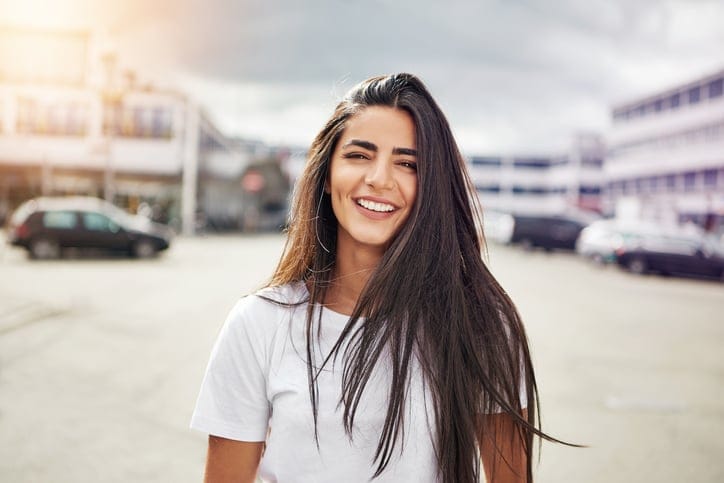 Smiling young woman in long brown hair and white short sleeve shirt walking in the middle of street