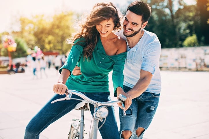 Young man helping his girlfriend riding a bike, outdoors at sunny location.