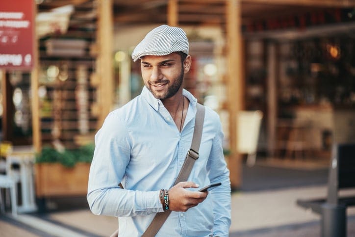 Young man holding a smart phone and walking on the street, looking away.