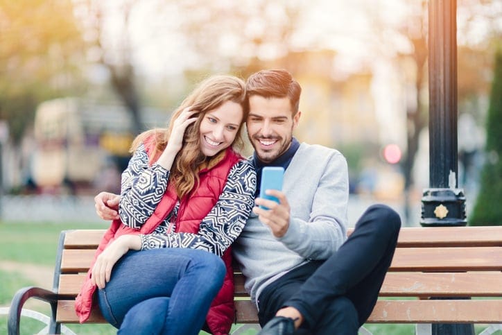 Young couple resting in the park and using smartphone