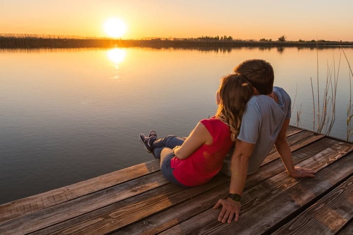 Back view of relaxed couple enjoying on a pier at sunset and looking at the view. Copy space.