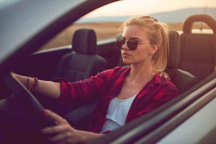 Beautiful young woman with sunglasses driving a cabrio.