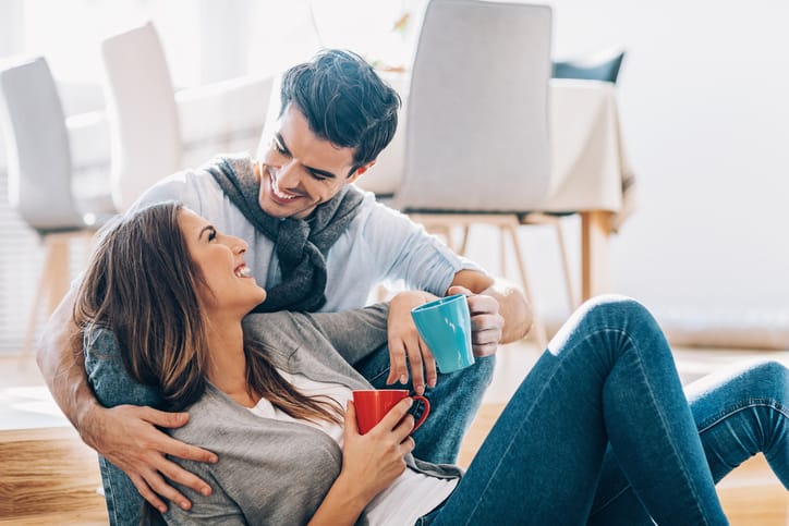 Young lovely couple on the floor, smiling and drinking coffee.