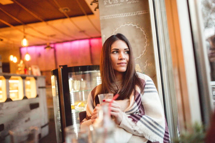 Young woman sitting in the cafe for a drink and looking through the window