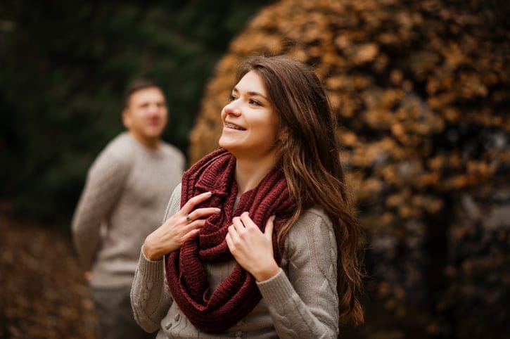Smiling girl with braces. Yong couple wearing on tied warm sweaters hugging in love at city in autumn background yellow bushes and trees.