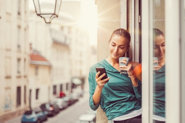 Smiling woman using smartphone and drinking coffee in the morning.