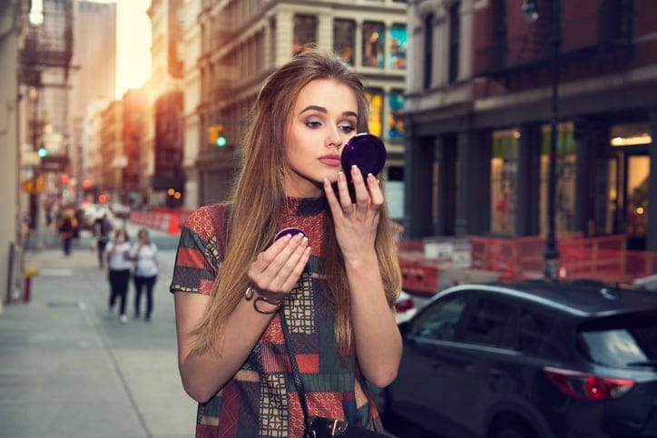 Woman doing her makeup and walking on city street.