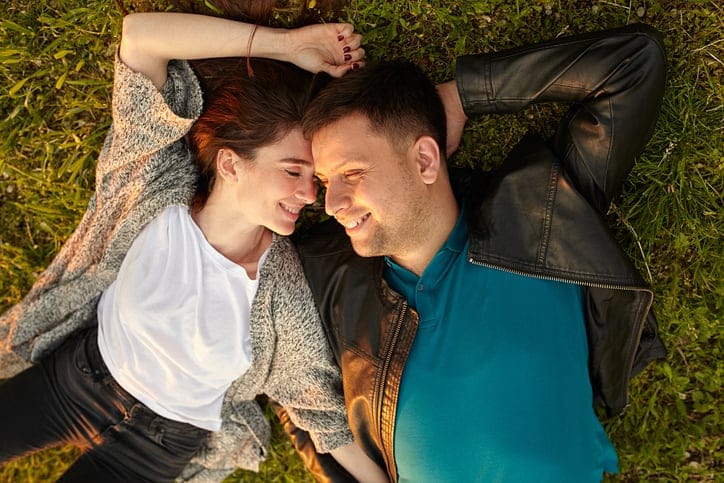Happy couple. fine portrait of young couple from above laughing and lying on grass at sunset