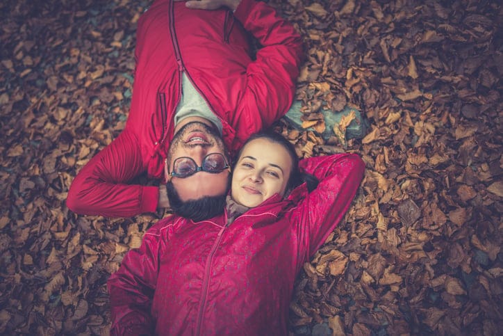 Smiling Couple Lying Down on Autumn Leaves Carpet in the forest.