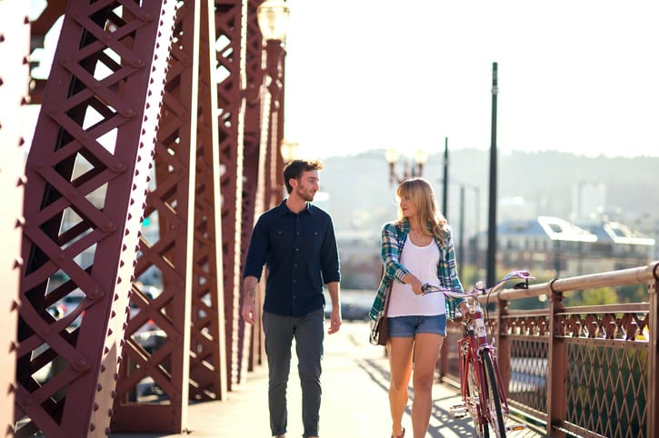Young adult heterosexual couple walking a bike along a bridge