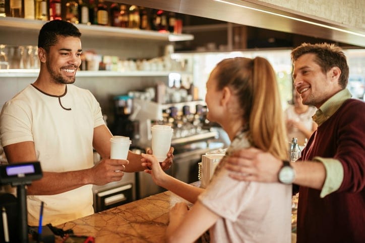Close up photo of a waiter serving a young couple take-away coffee