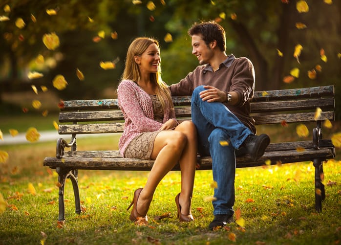 Beautiful young couple sitting on park bench and smiling.Autumn concept.
