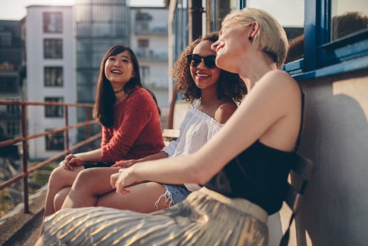 Three young female friends sitting in balcony and having fun. Women relaxing outdoors and chatting.