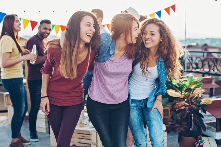 Three girls holding and laughing on a rooftop celebration.