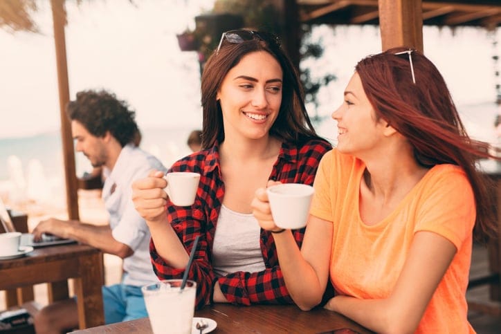 Two friends drinking coffee and having fun at a beach bar.