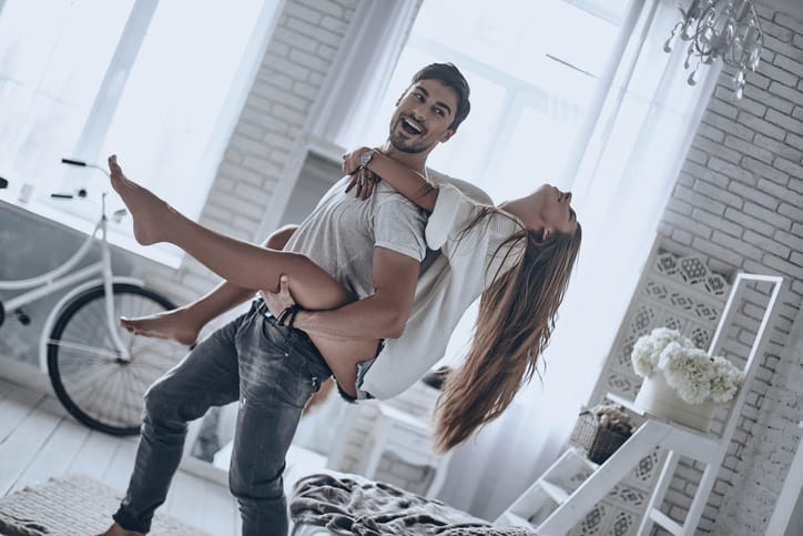Young beautiful couple having fun at home together while man carrying his girlfriend on shoulders